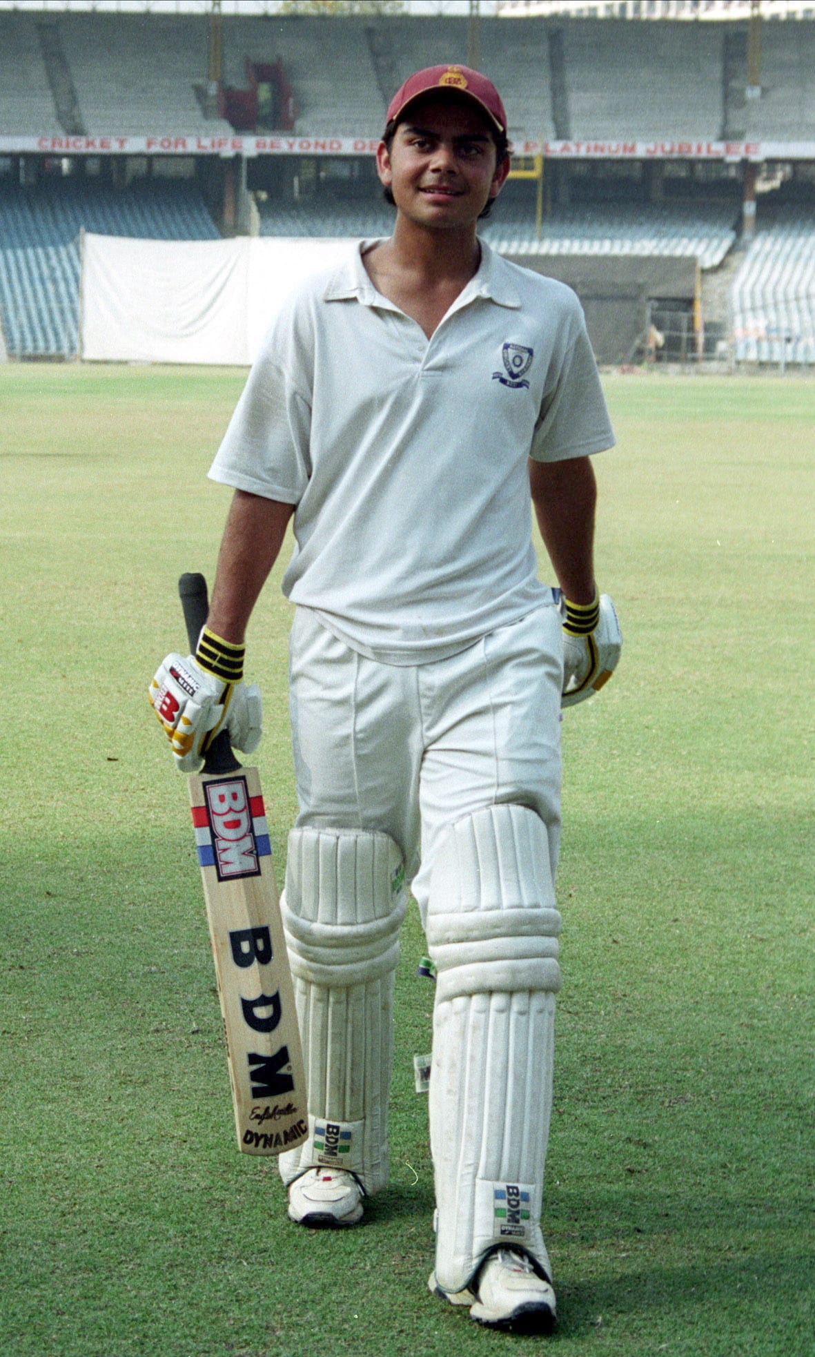 Historic Delhi Ranji Trophy debut photograph of 18-year-old Virat Kohli in white flannels and maroon cap walking off Feroz Shah Kotla pitch with BDM bat and pads, 2006