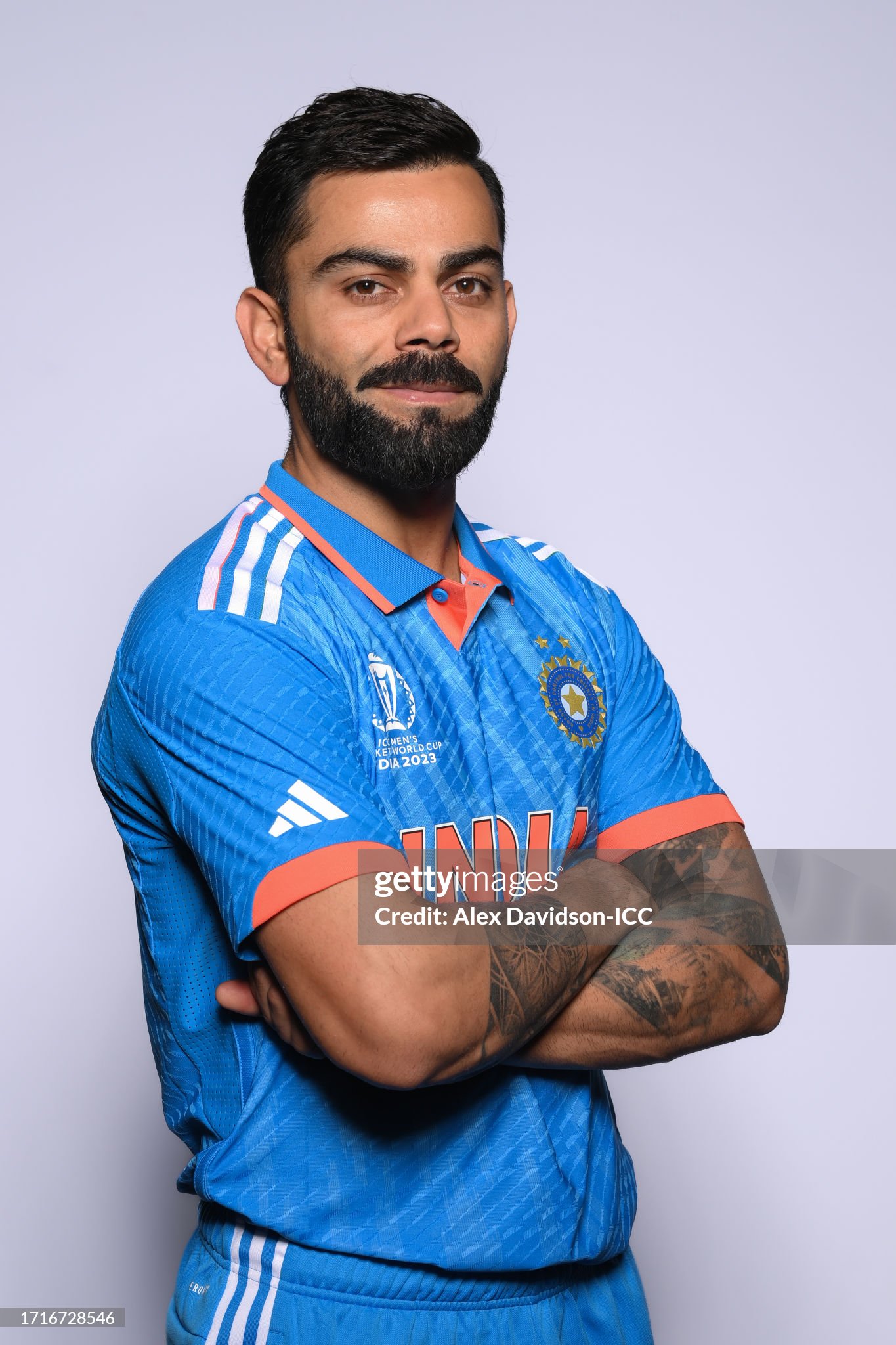 Virat Kohli standing with folded arms and tattooed forearms in moody chiaroscuro studio lighting